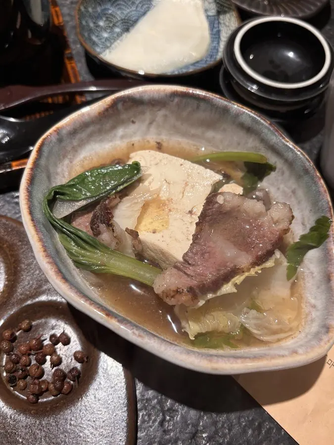 A bite of hanwoo wrapped with mushroom and bok choy, dipped in sauce