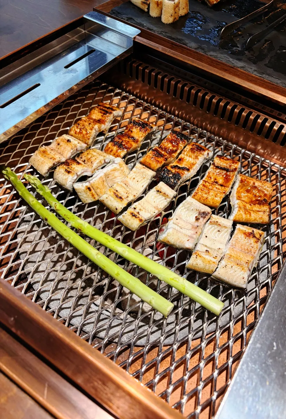 Asparagus grilling on the tabletop grill alongside eel
