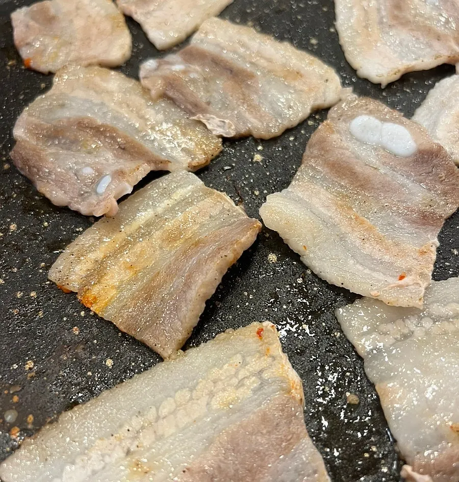 Frozen pork belly grilling with pepper sprinkled on top