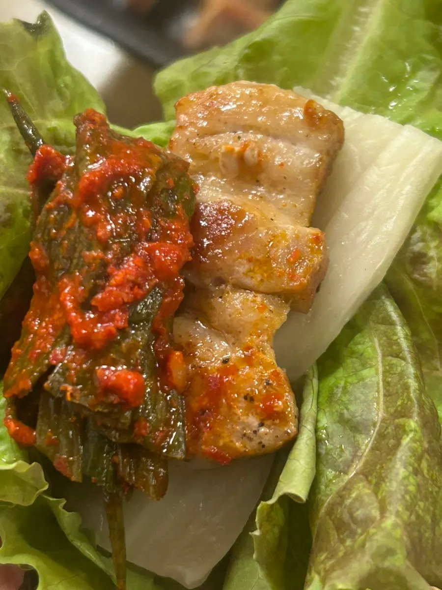 A lettuce wrap with meat and green onion kimchi