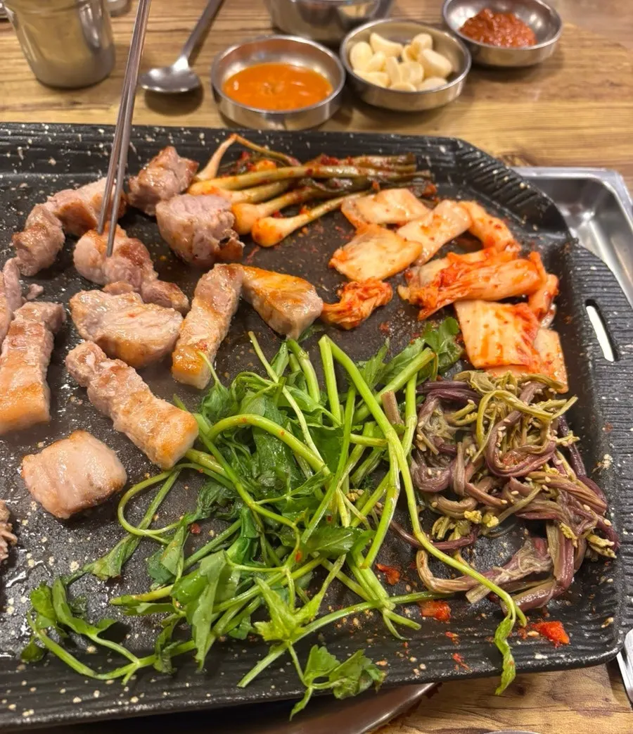 Pork belly cooking on the grill with side dishes