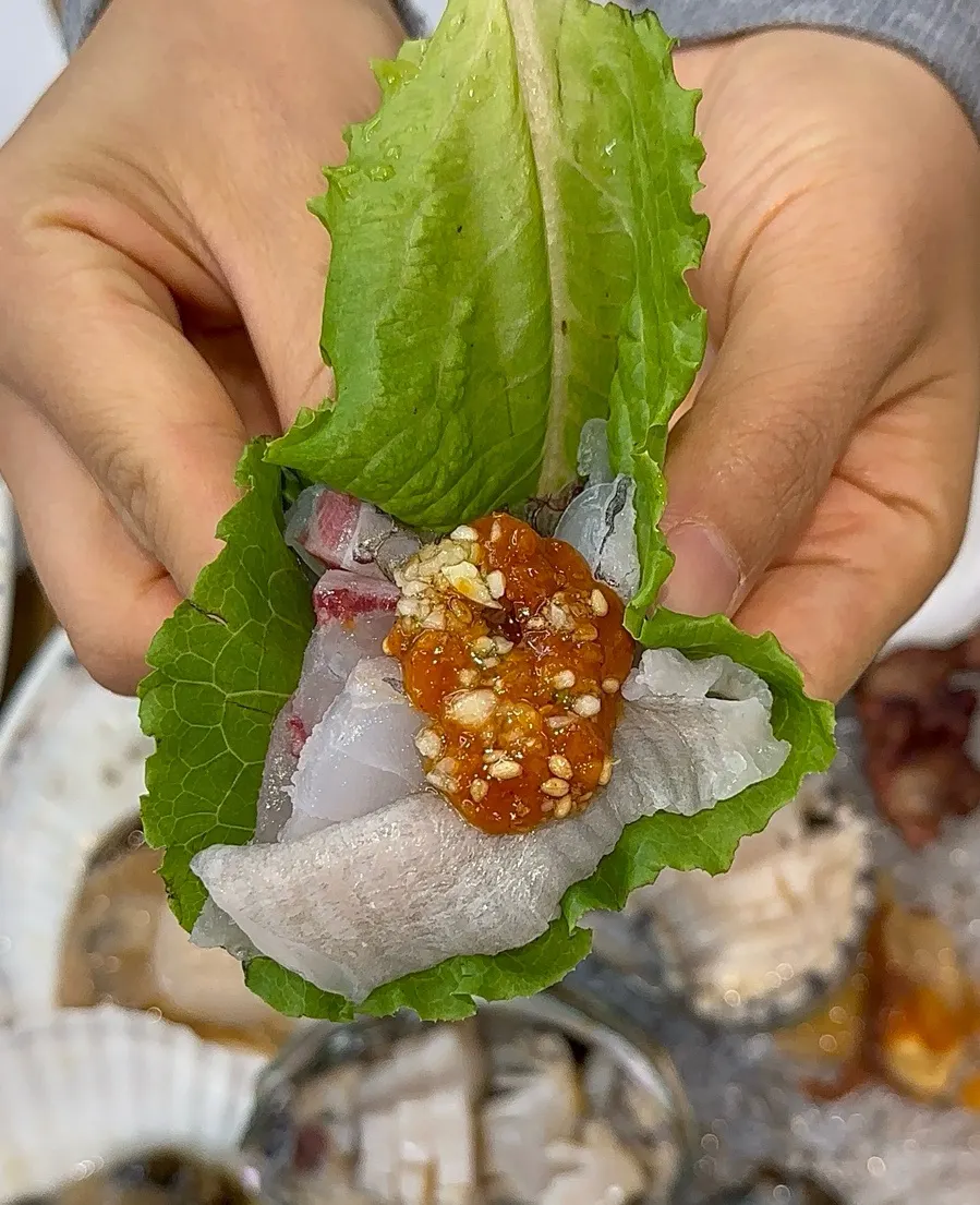 A wrap of sashimi, garlic and ssamjang on a perilla leaf