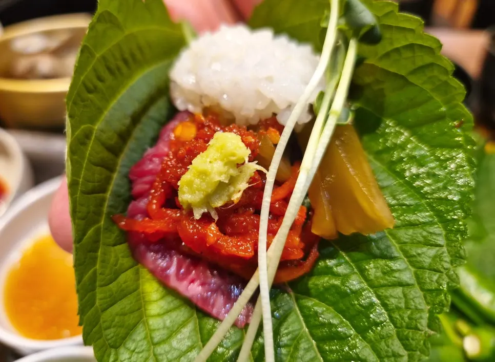 A bite of raw beef sashimi wrapped in perilla leaf