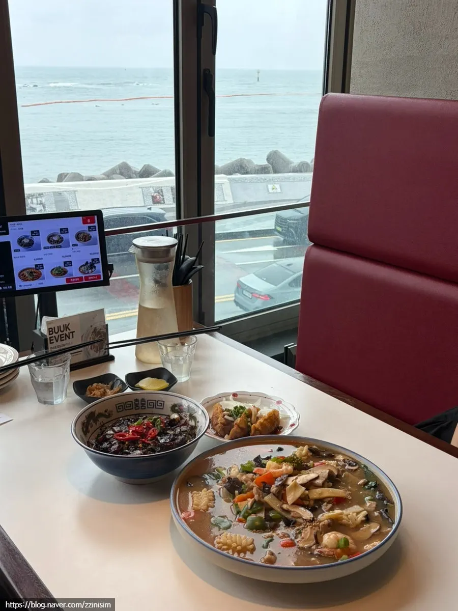 Table spread of seafood nurungji-tang and gochu ganjajang with the sea in the background