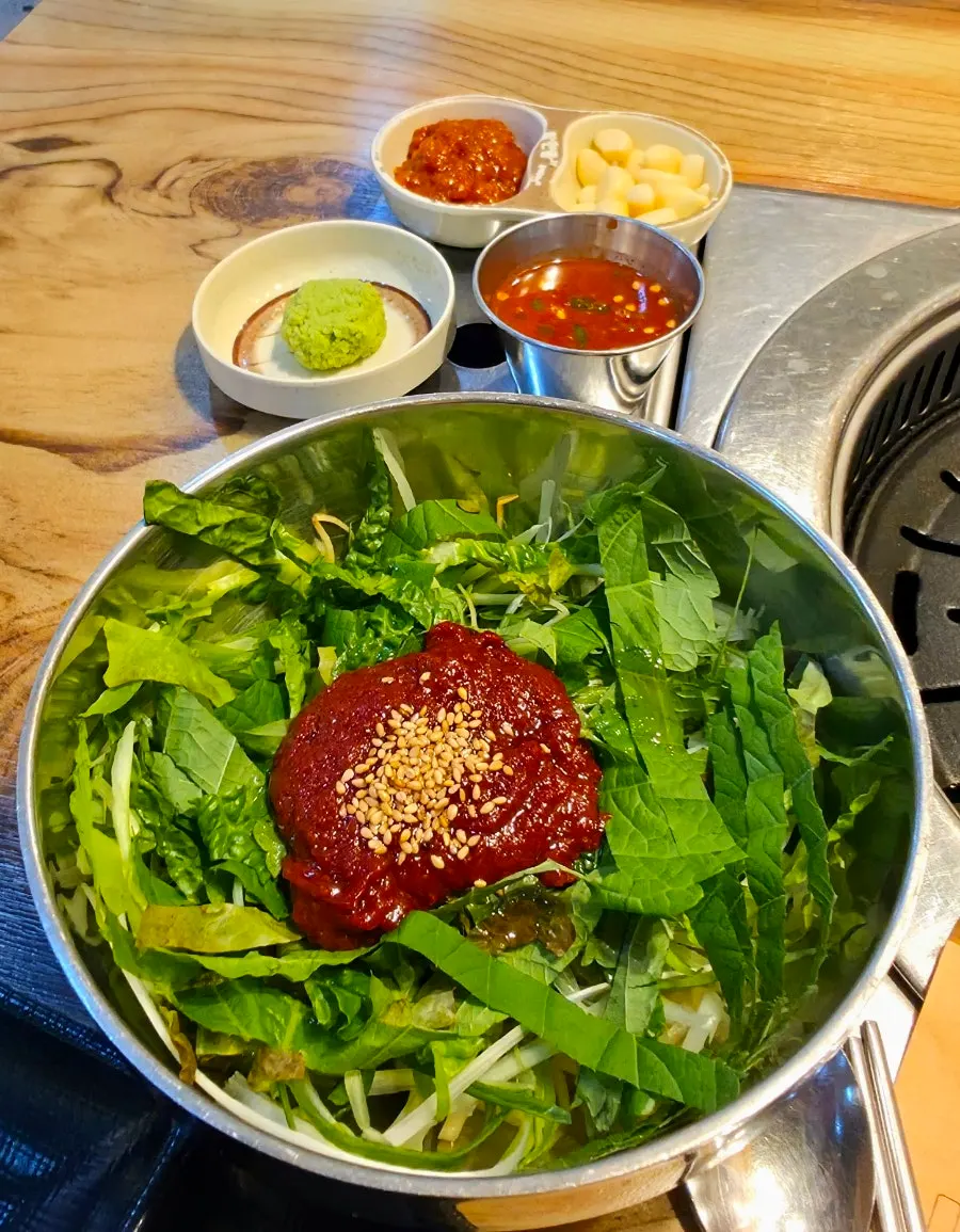 A basket of lettuce and perilla leaves with geotjeori in a steel bowl