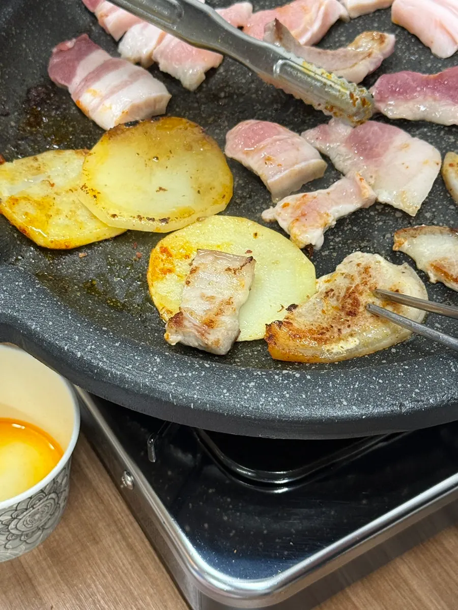 鉄板にジャガイモとニンニクを一緒にのせて焼く五枚肉
