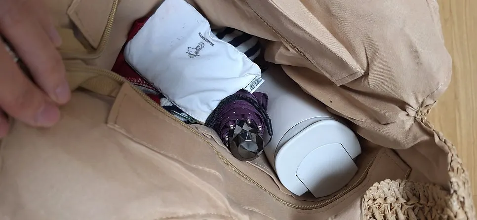 Rattan shoulder bag holding a tumbler and pouch