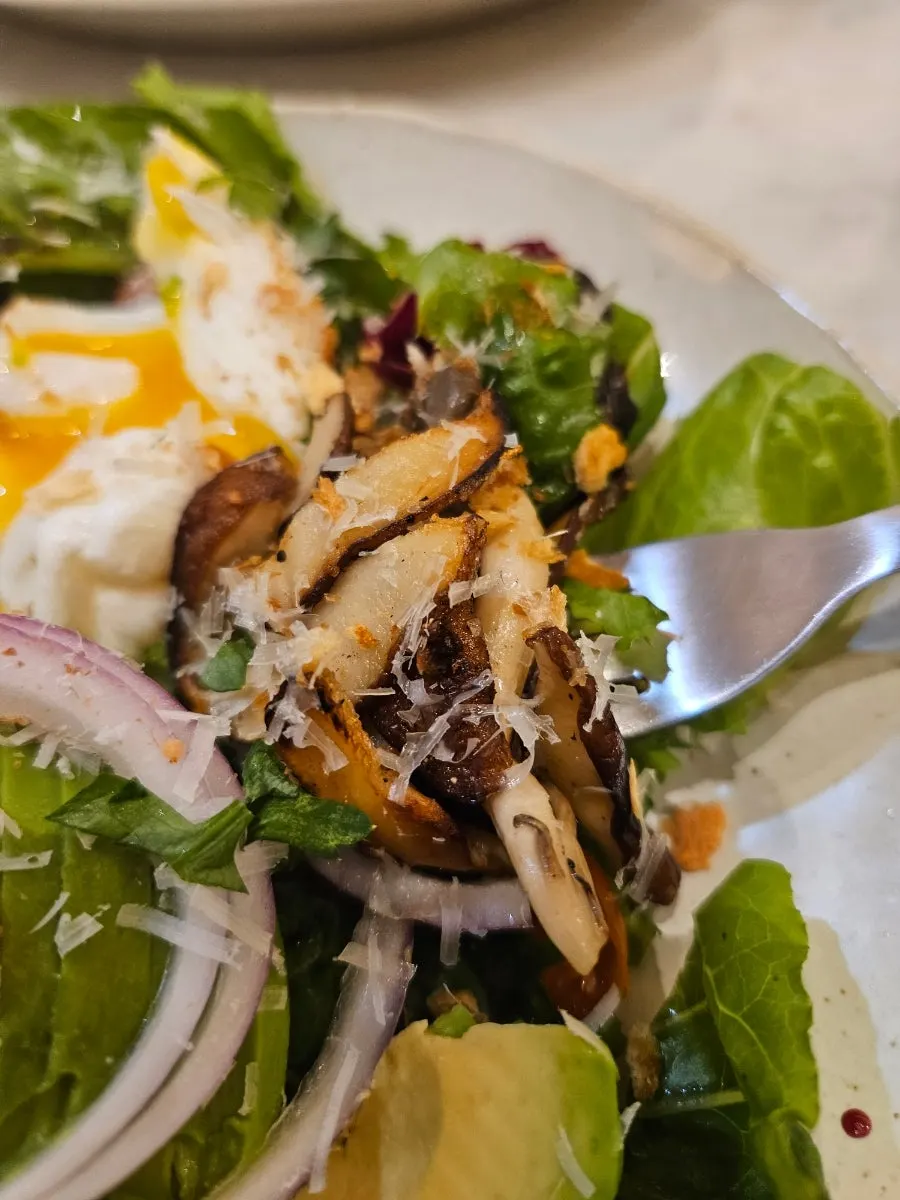 Salad topped with avocado, grilled mushrooms, and poached egg