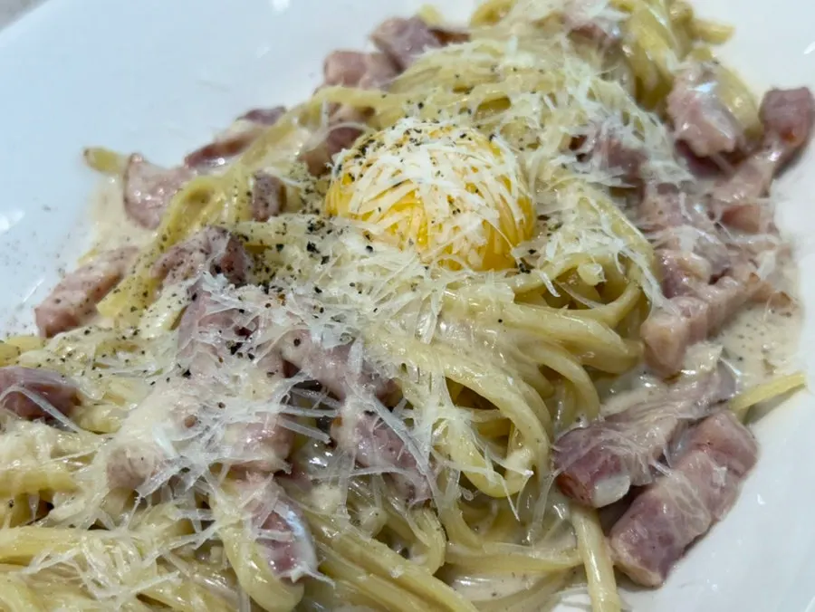 Carbonara topped with egg yolk and bacon
