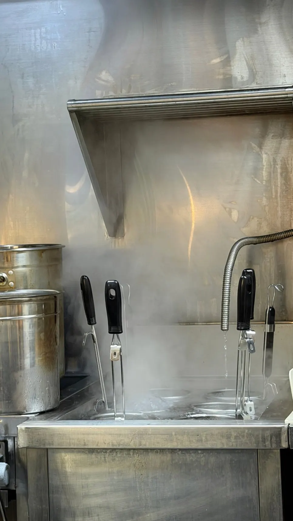 Steam rising from the noodle-boiling pot in the ramen shop kitchen