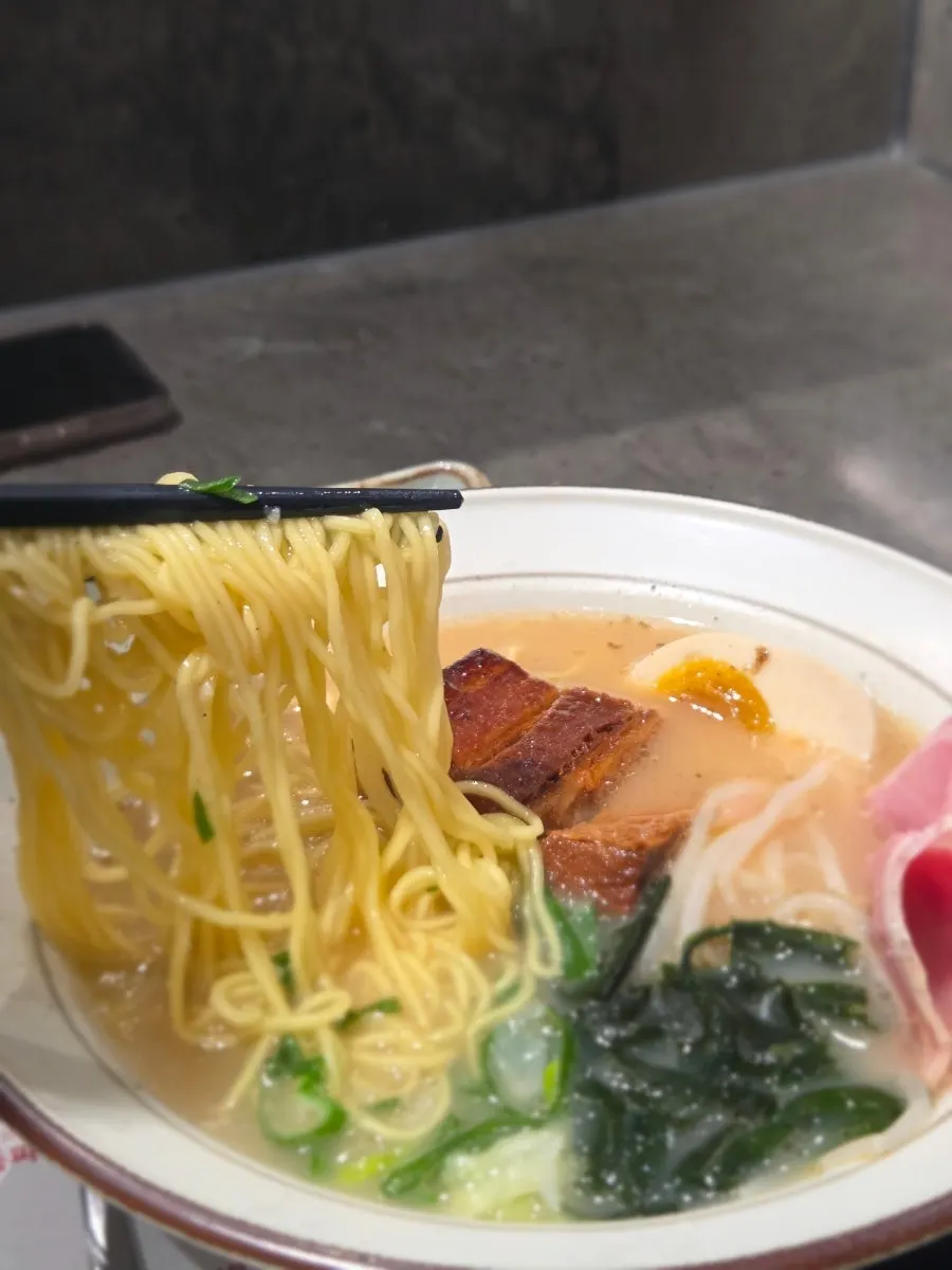 Thin noodles lifted out of the milky-white broth