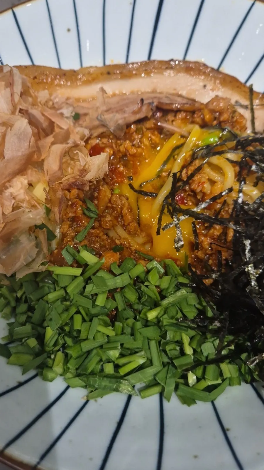 Chopsticks lifting noodles with a piece of pork belly on top