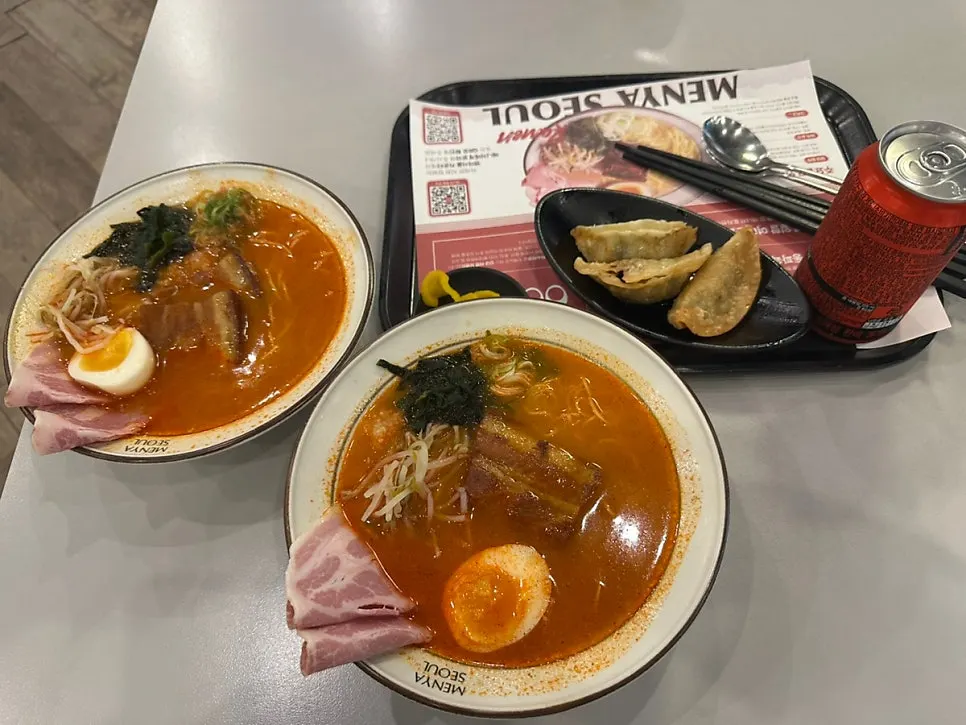 Two bowls of spicy ramen and sides on a food court table