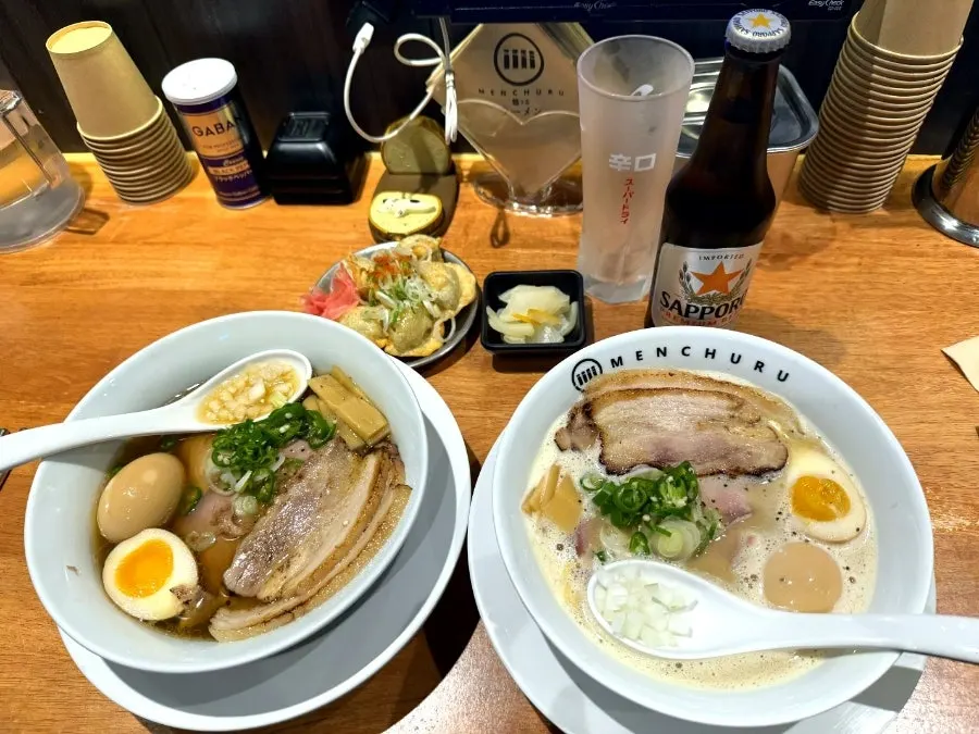Two bowls of ramen, fried gyoza, and a Sapporo bottled beer on the table