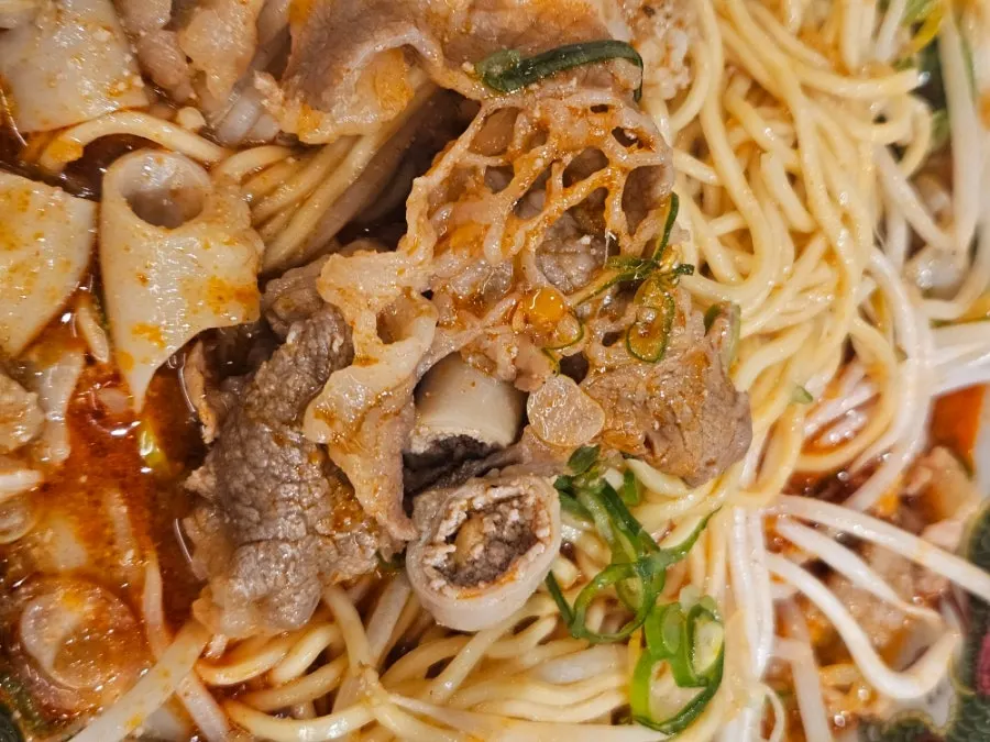 Gambar dekat mi dan sukju dalam motsu ramen