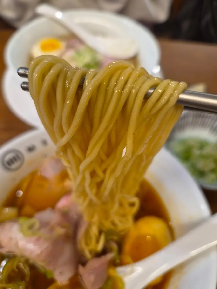 Spicy shoyu ramen noodles lifted with chopsticks