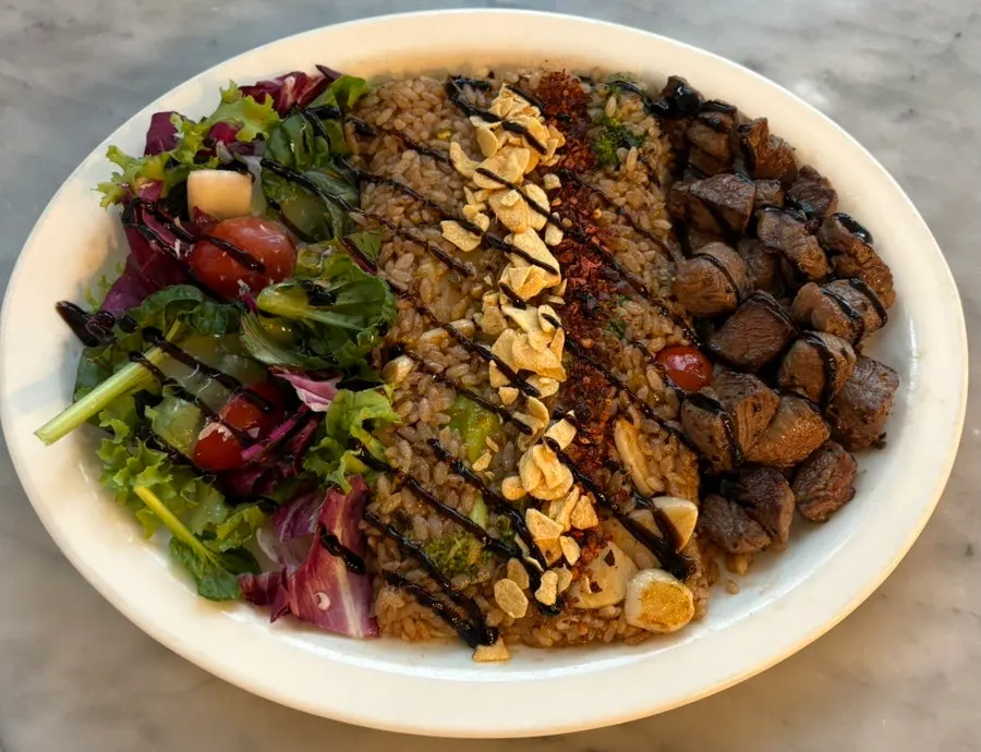 Satu piring pilaf berisi cube steak, nasi goreng, dan salad