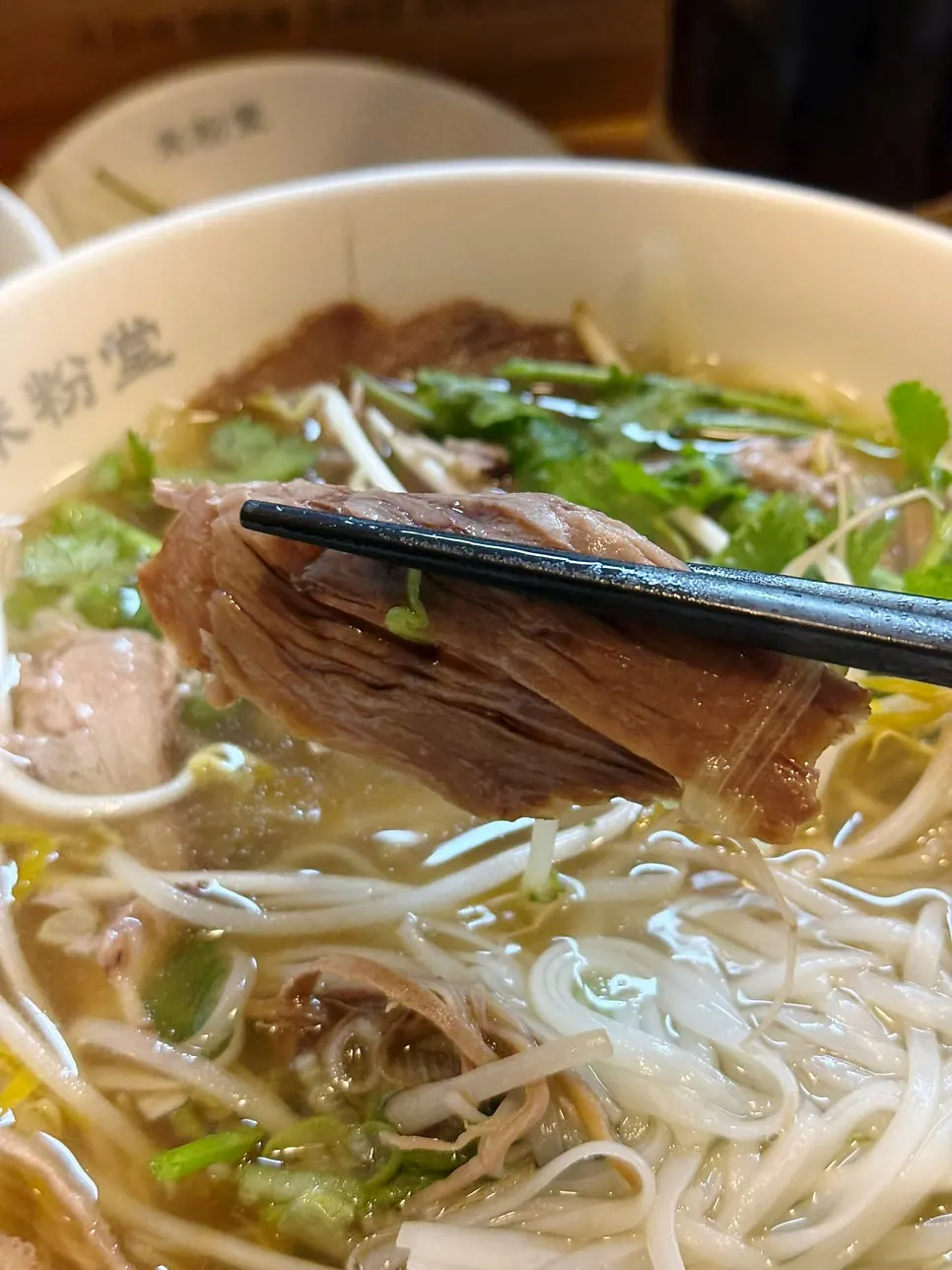 A piece of meat lifted with chopsticks from the pho