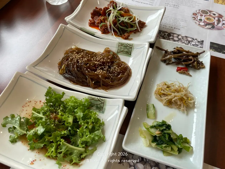 Neatly arranged side dishes including stir-fried pork and japchae