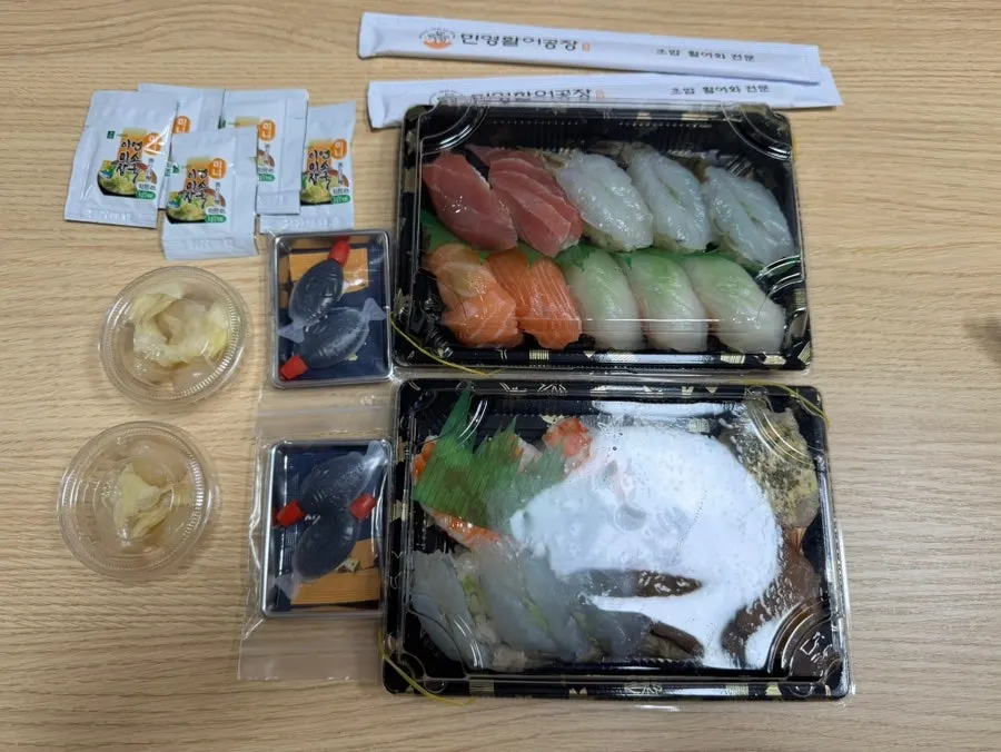 Two sushi packs laid out on the table with sides