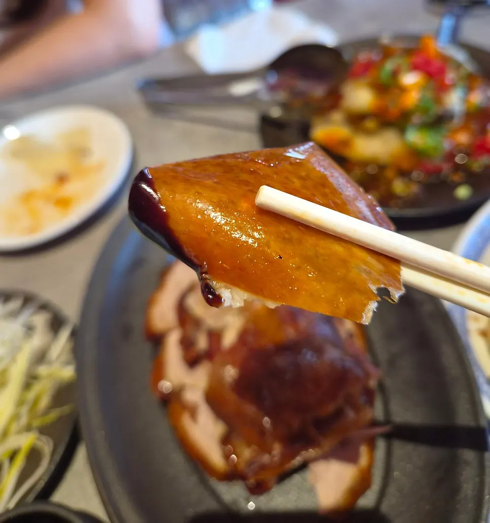 A piece of Peking duck picked up with chopsticks