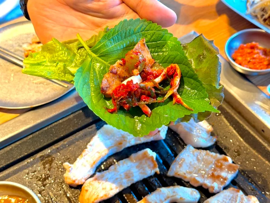 A lettuce wrap with meat, garlic, and olive kimchi