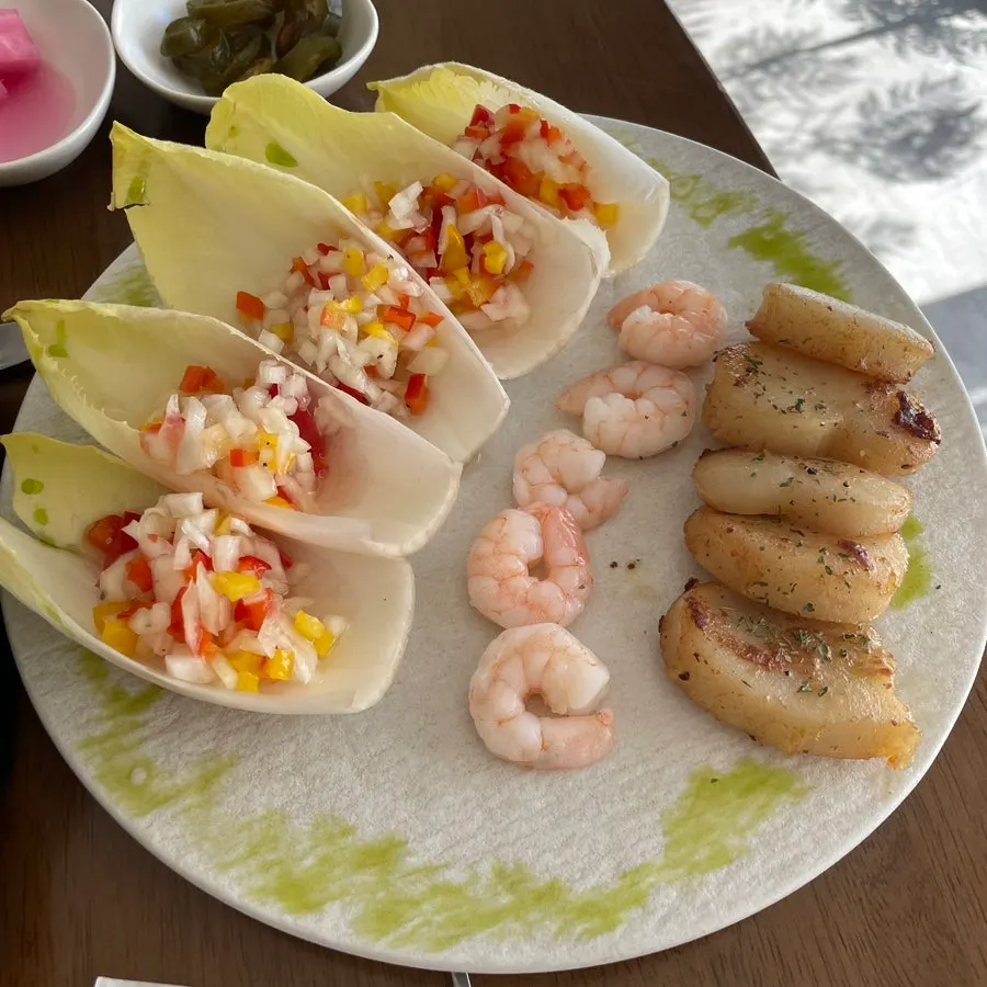 A single bite with scallop and cocktail shrimp on an endive leaf