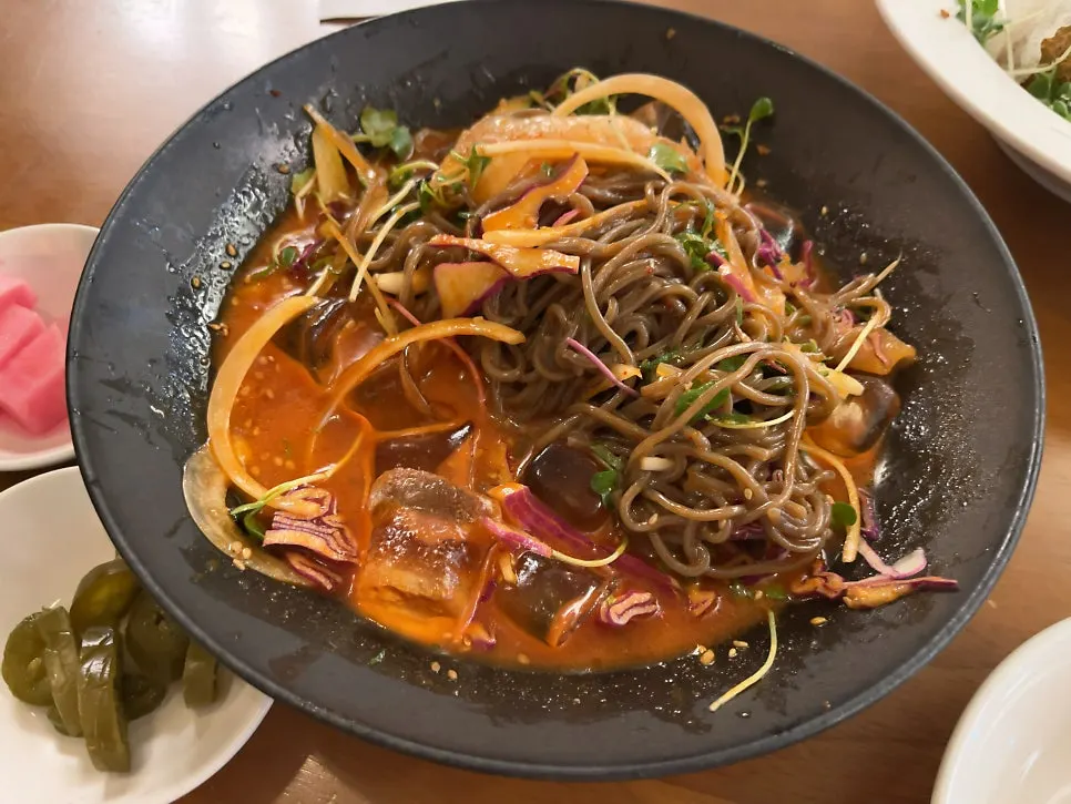 A chopstick-full of spicy buckwheat noodles with flounder on the table