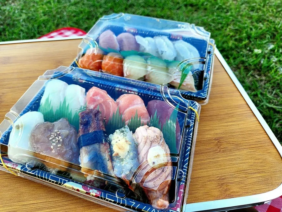 Packed sushi and market snacks laid out at the park