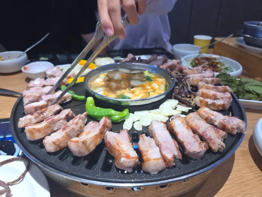 Thick pork belly and neck on the grill with a pot of doenjang jjigae in the center