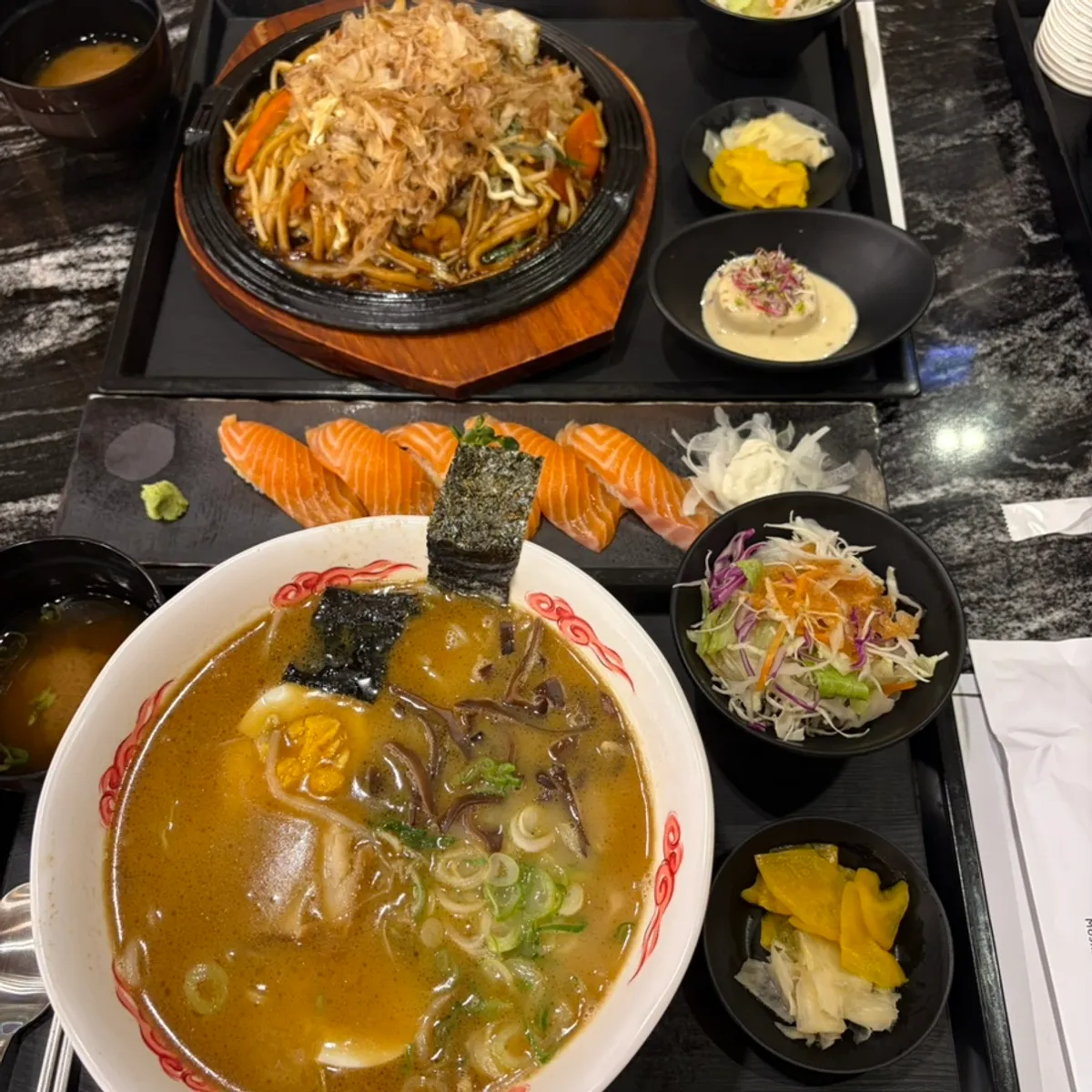 Table with salmon sushi, ramen, and yaki udon together