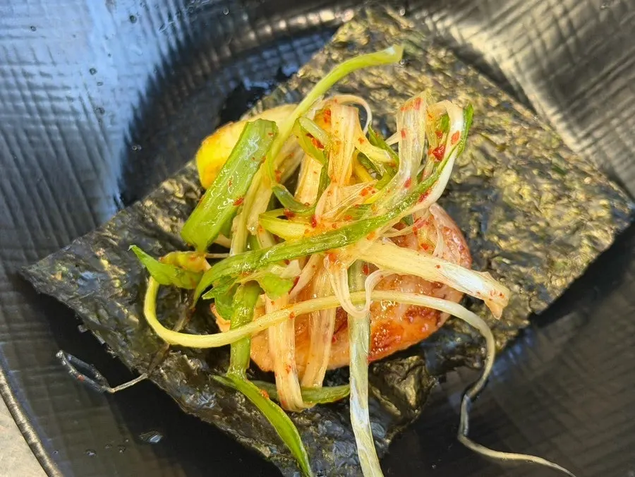 A wrap of seaweed, meat, soy sauce, and scallion