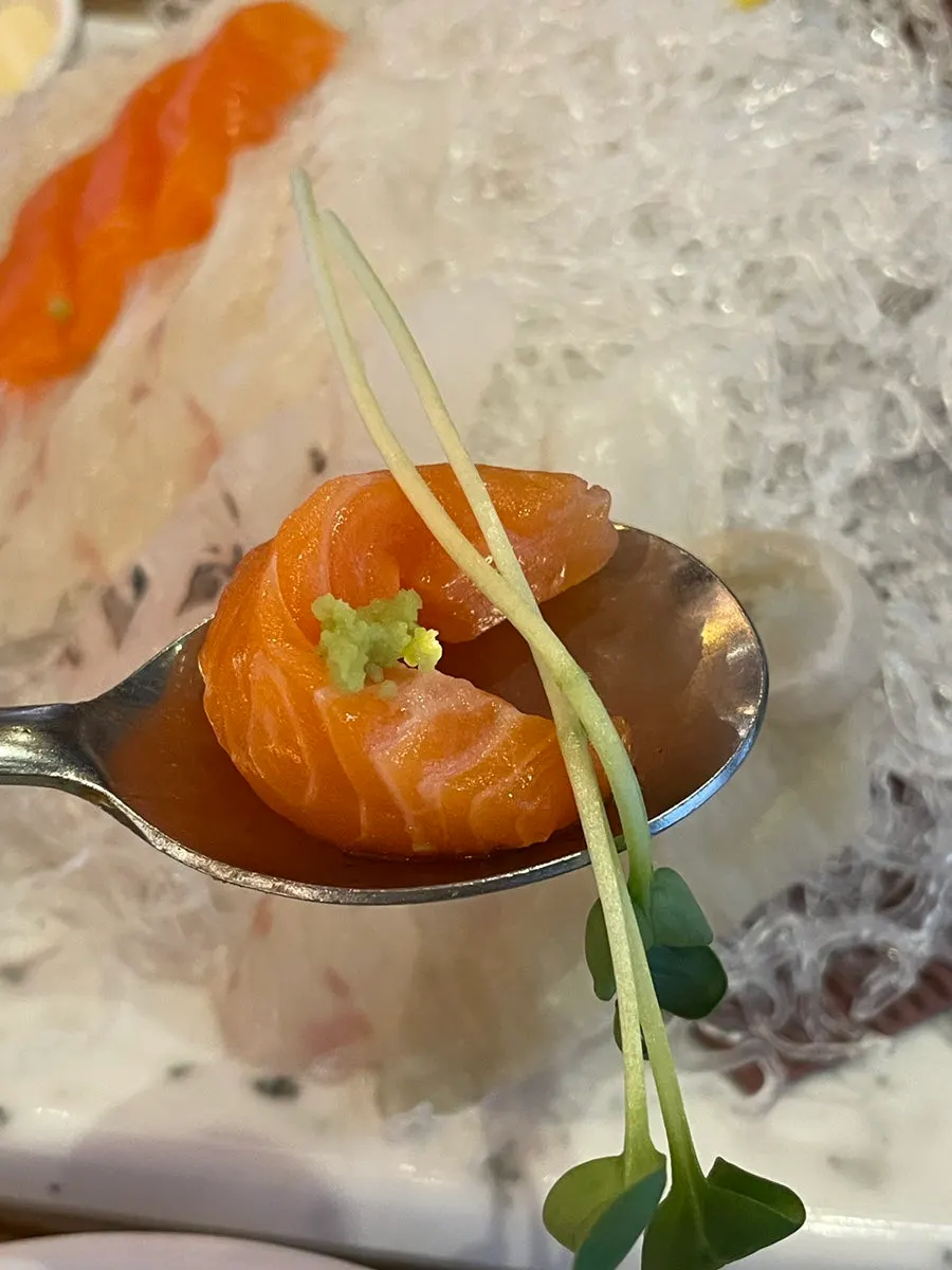 A piece of sashimi topped with wasabi and radish sprouts
