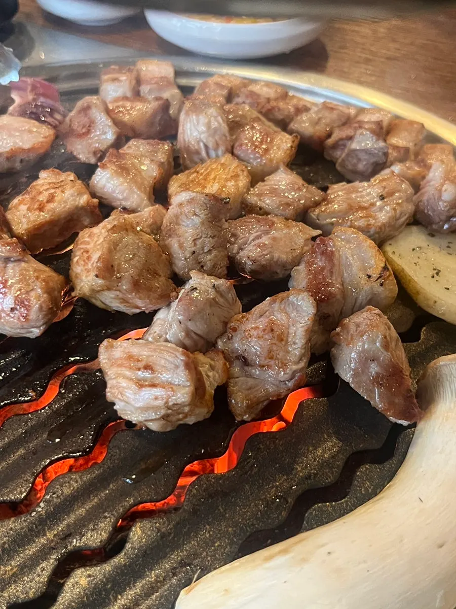 Staff member grilling meat along with onion, mushroom, and potato