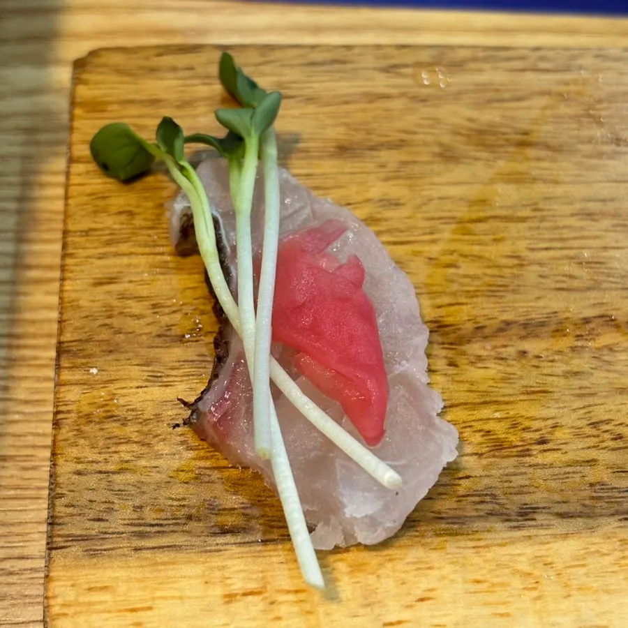 A piece of sashimi topped with radish sprouts and ginger