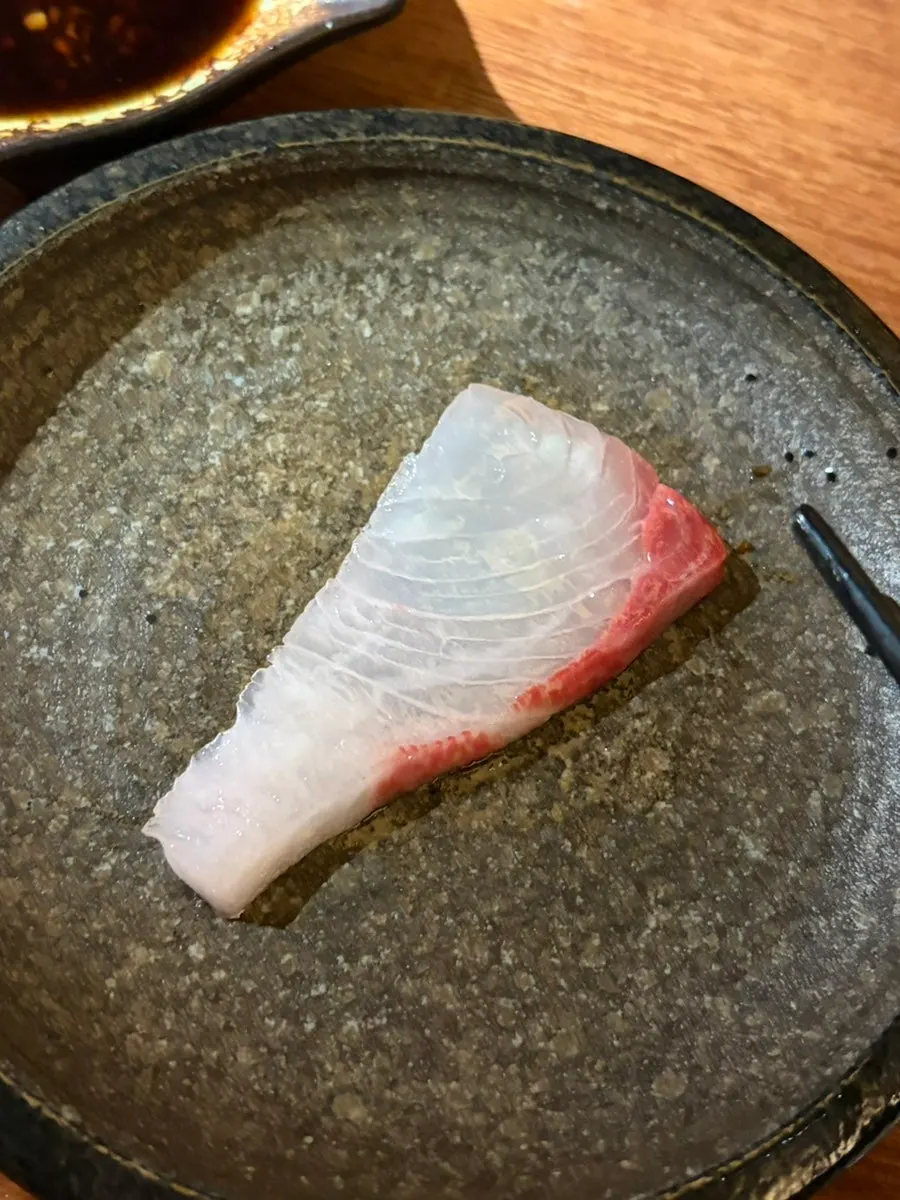 A piece of dry-aged sashimi picked up with chopsticks