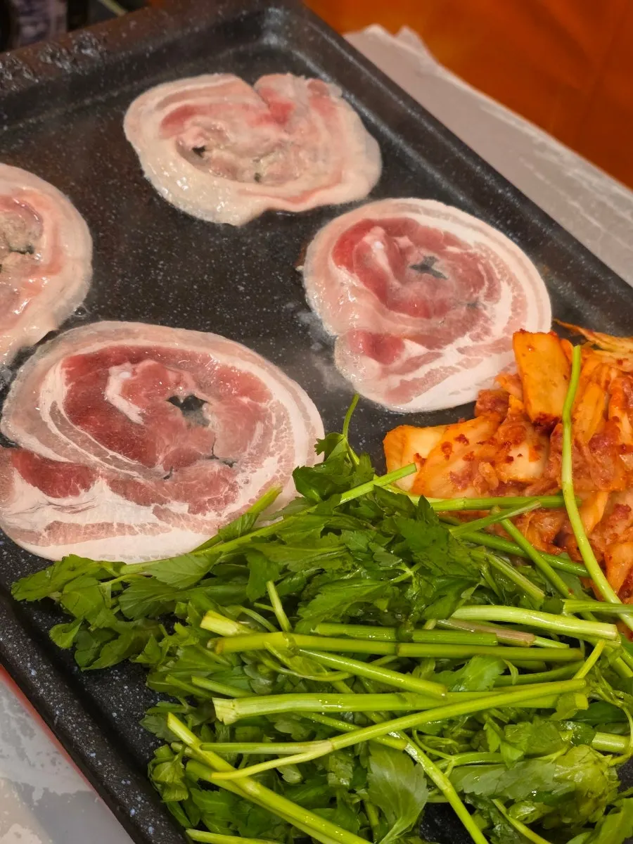 Minari and pork belly cooking together on the grill