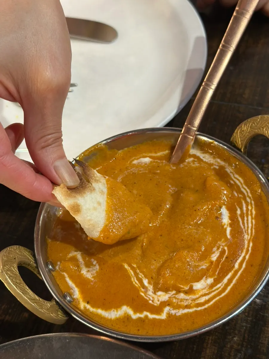 Naan dipped into butter chicken curry