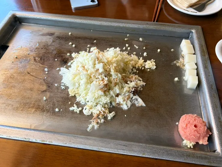 Mentaiko monjayaki ingredients piled on one side of the griddle