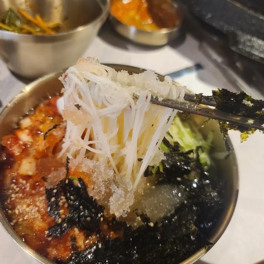 Noodles of kimchi-mari guksu topped with seaweed flakes and kimchi