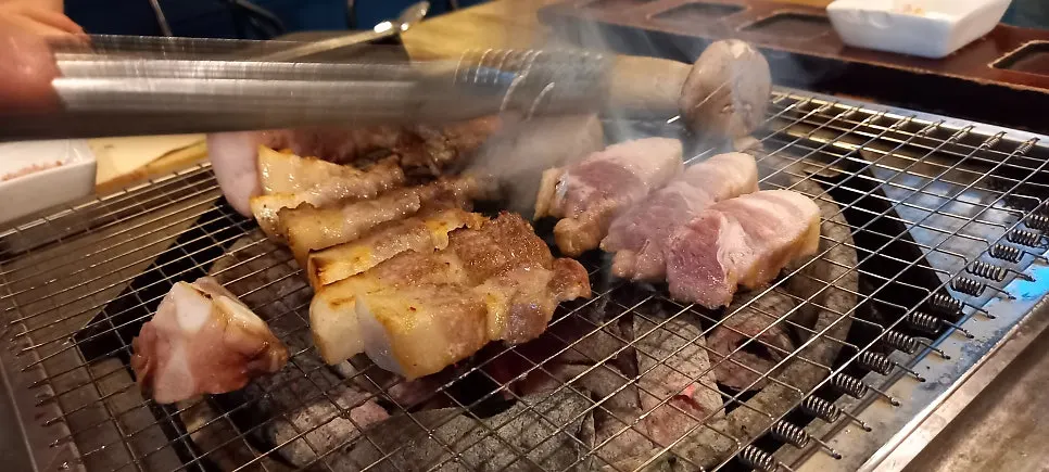 여러 조각의 돼지고기가 익는 숯불 불판