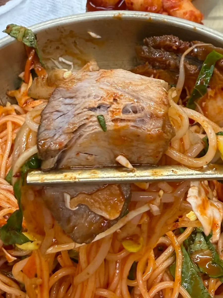 A bite of meat bibim guksu with noodles and vegetables