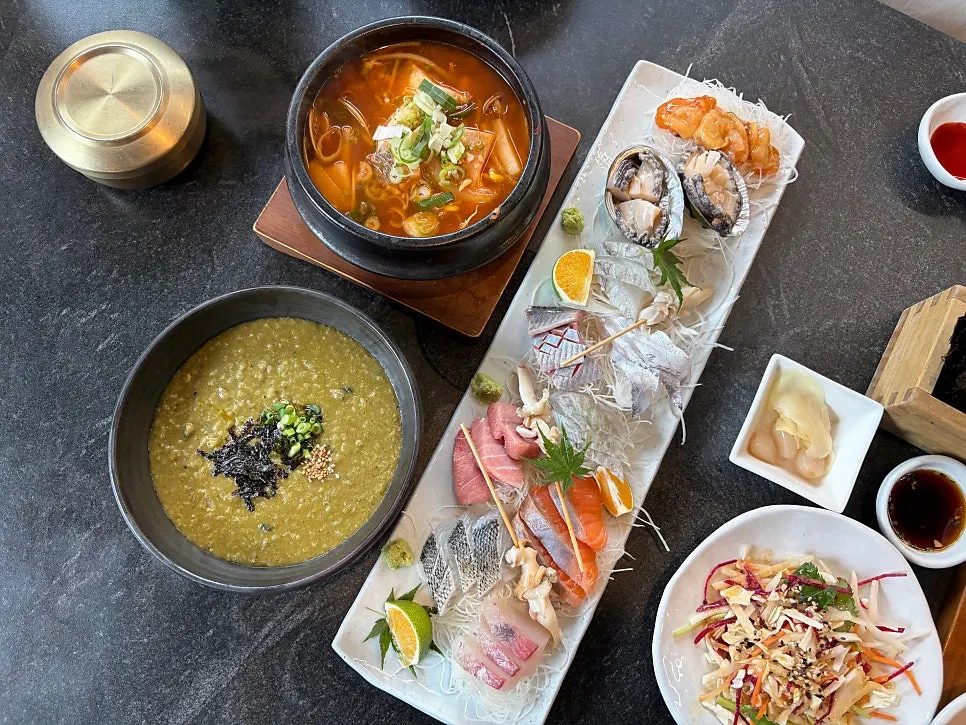 Table spread of bori-jjuk, croaker stew, and mixed sashimi
