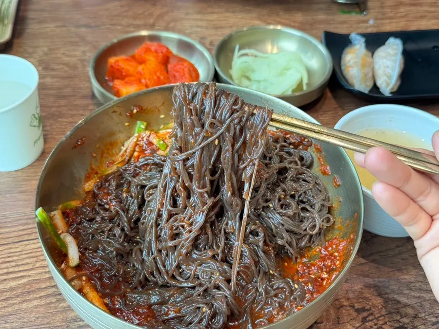 Chopsticks lifting a strand of bibim naengmyeon noodles