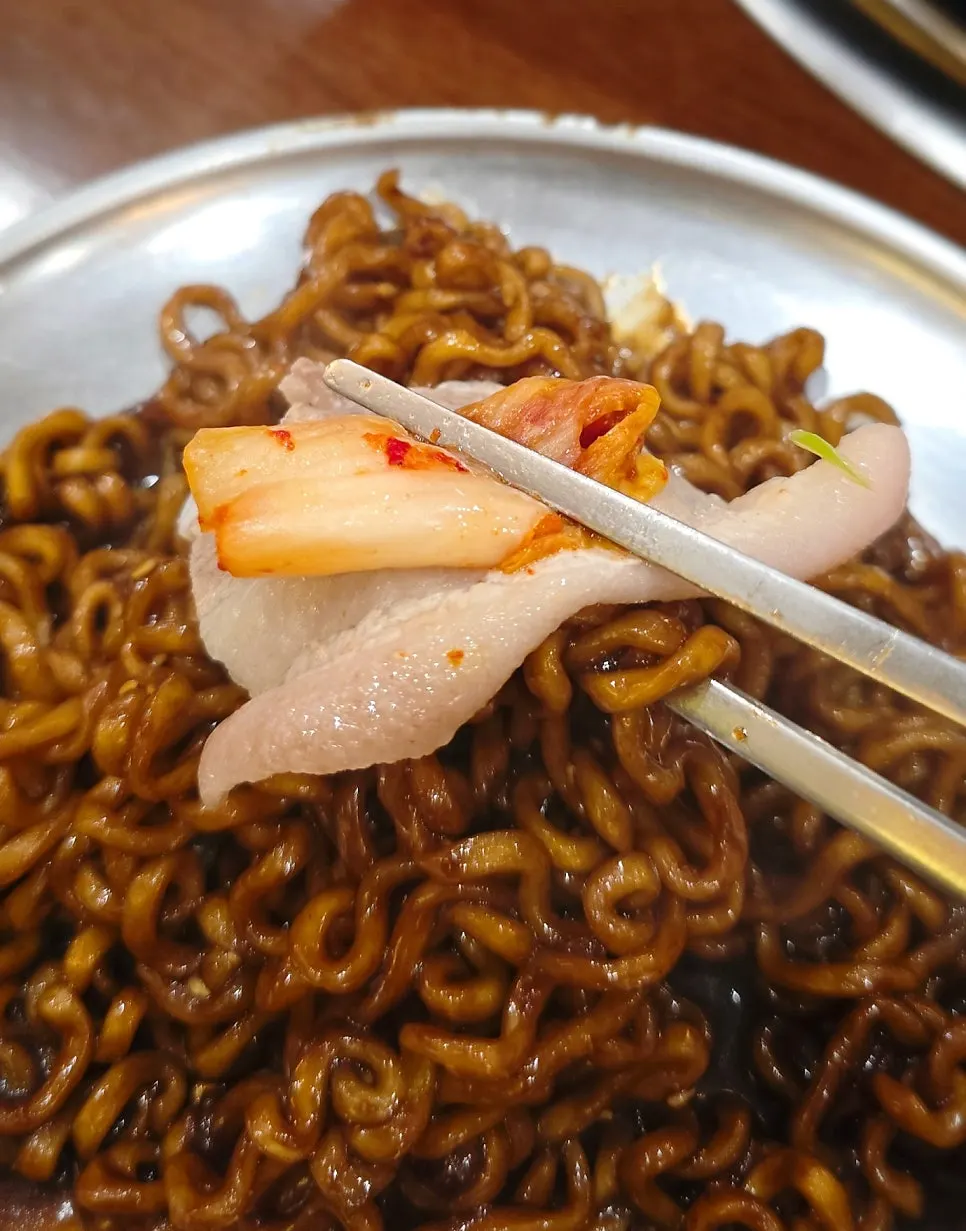 A bite of unpan japchaguetti topped with frozen pork belly
