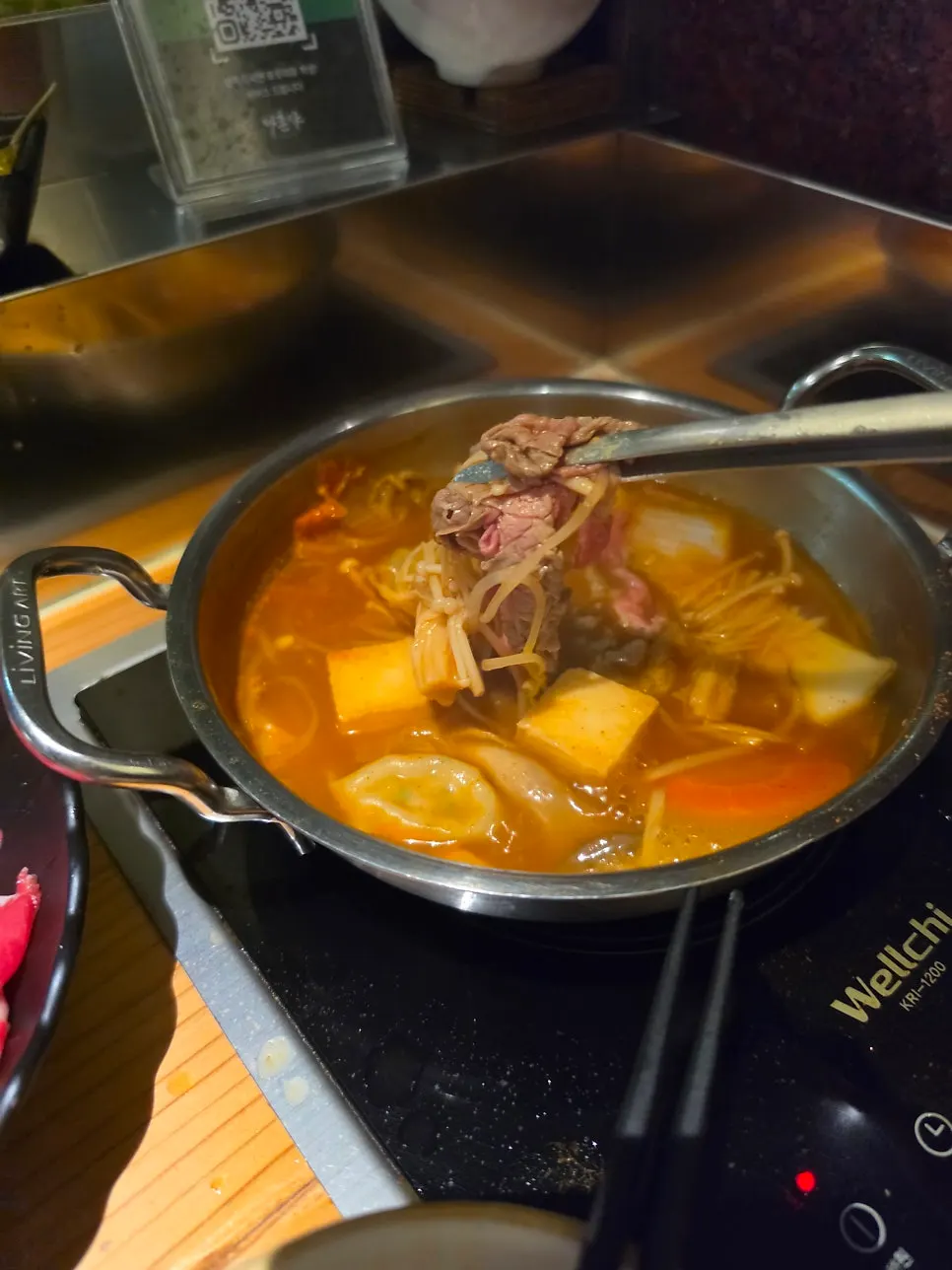 Cooked meat, vegetables, and tofu lifted out of the spicy shabu-shabu