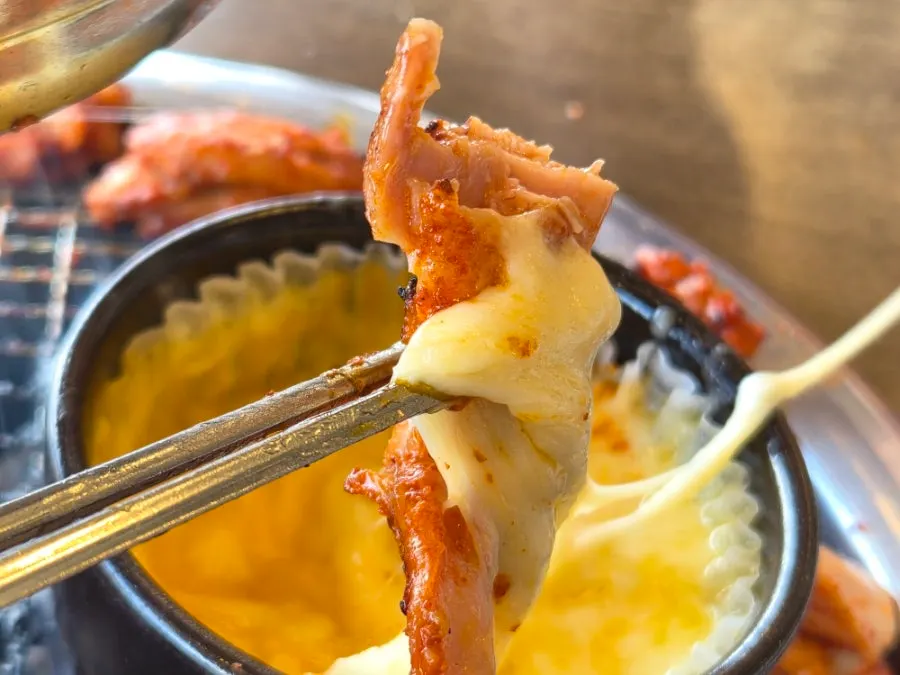 A piece of dakgalbi dipped in cheese fondue