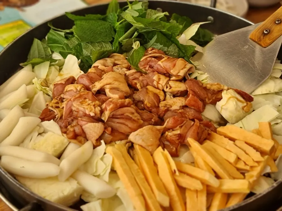 Hot plate with raw chicken, cabbage, rice cake, and sweet potato