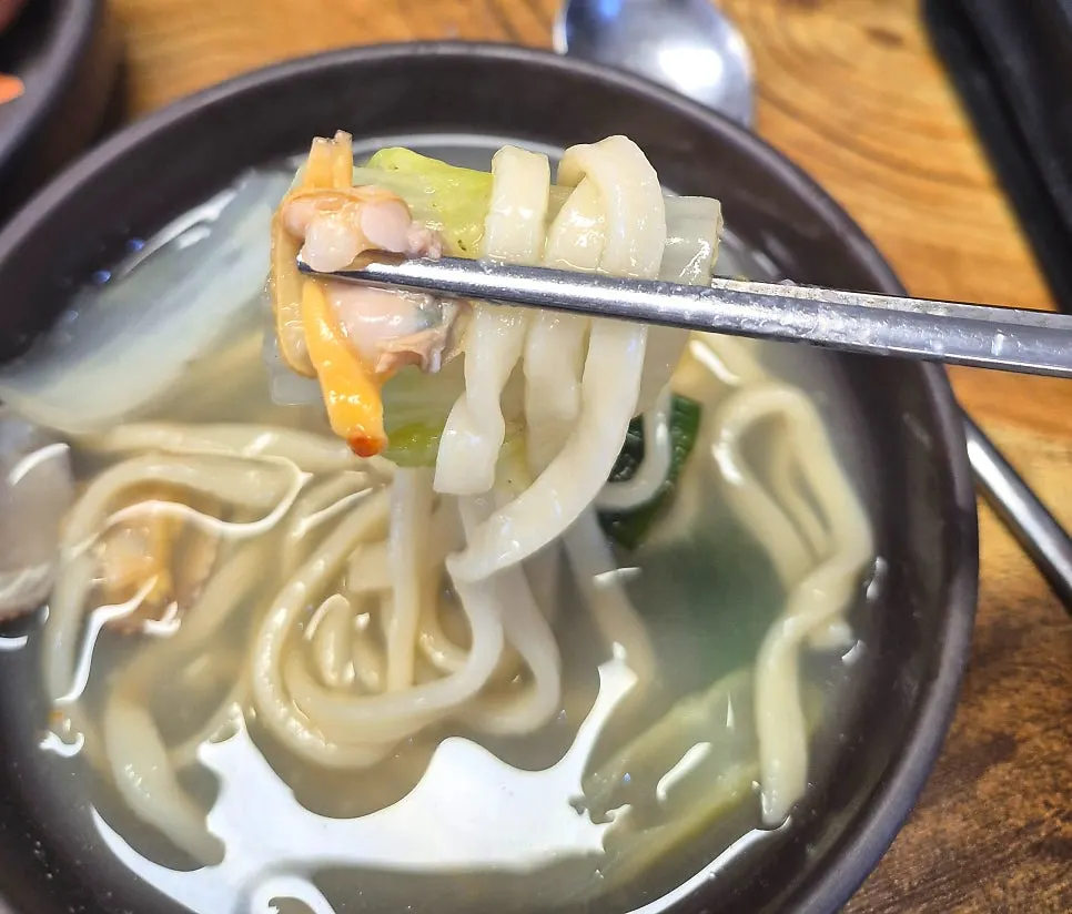 A bowl of kalguksu broth served with kimchi