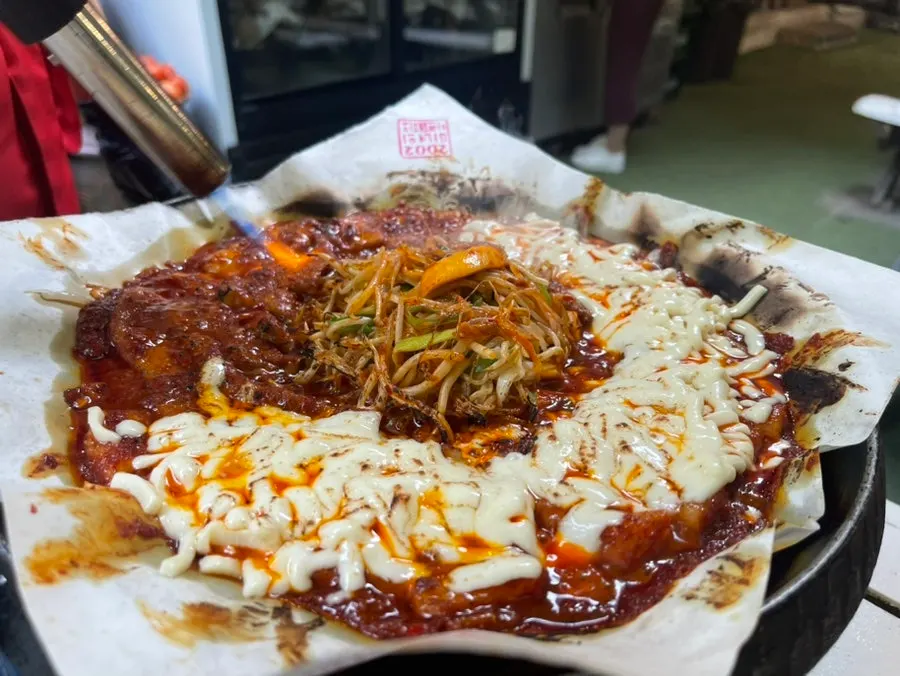 Torch fire show over cheese-topped pork belly